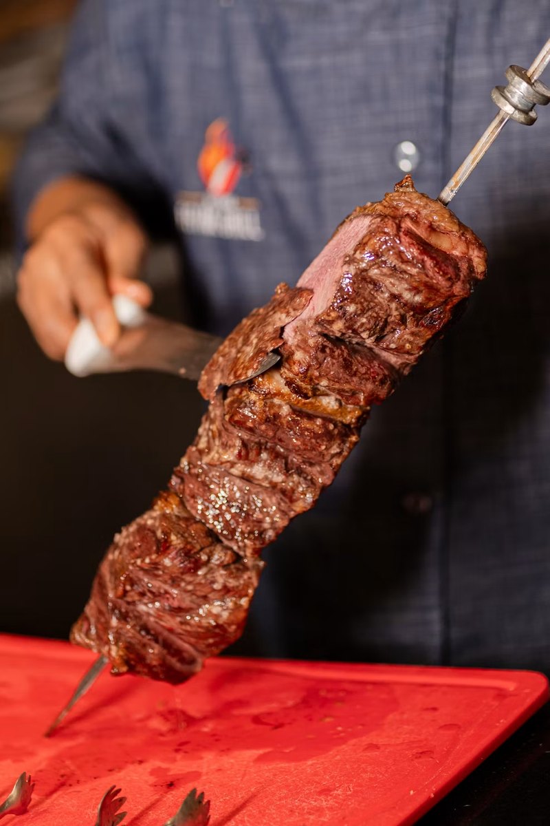 Tucanos - An image of meet being cut on a skewer.